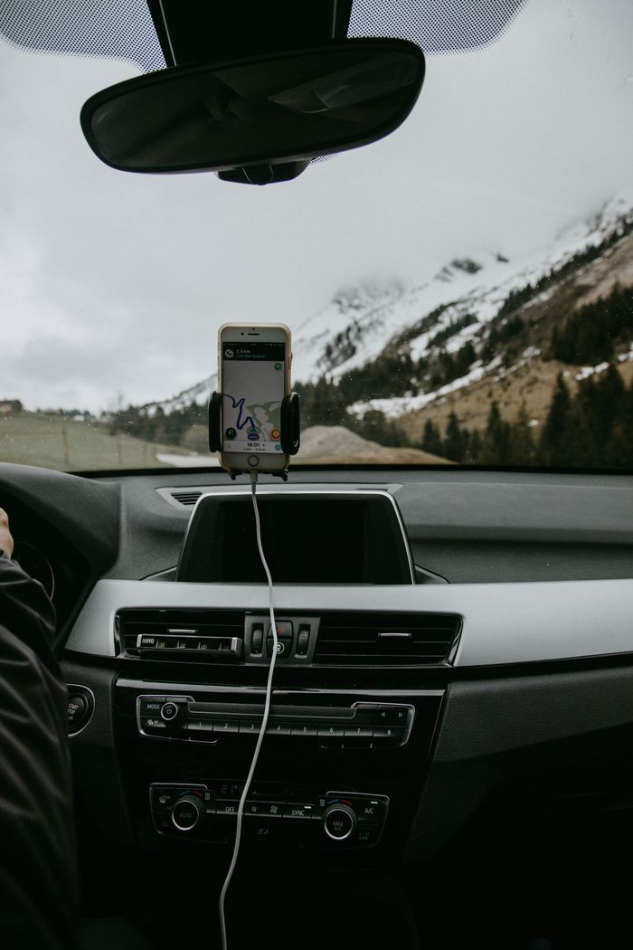 process-img Driver in car with smartphone showing route due to GPS against snowy hill slope with coniferous trees and road